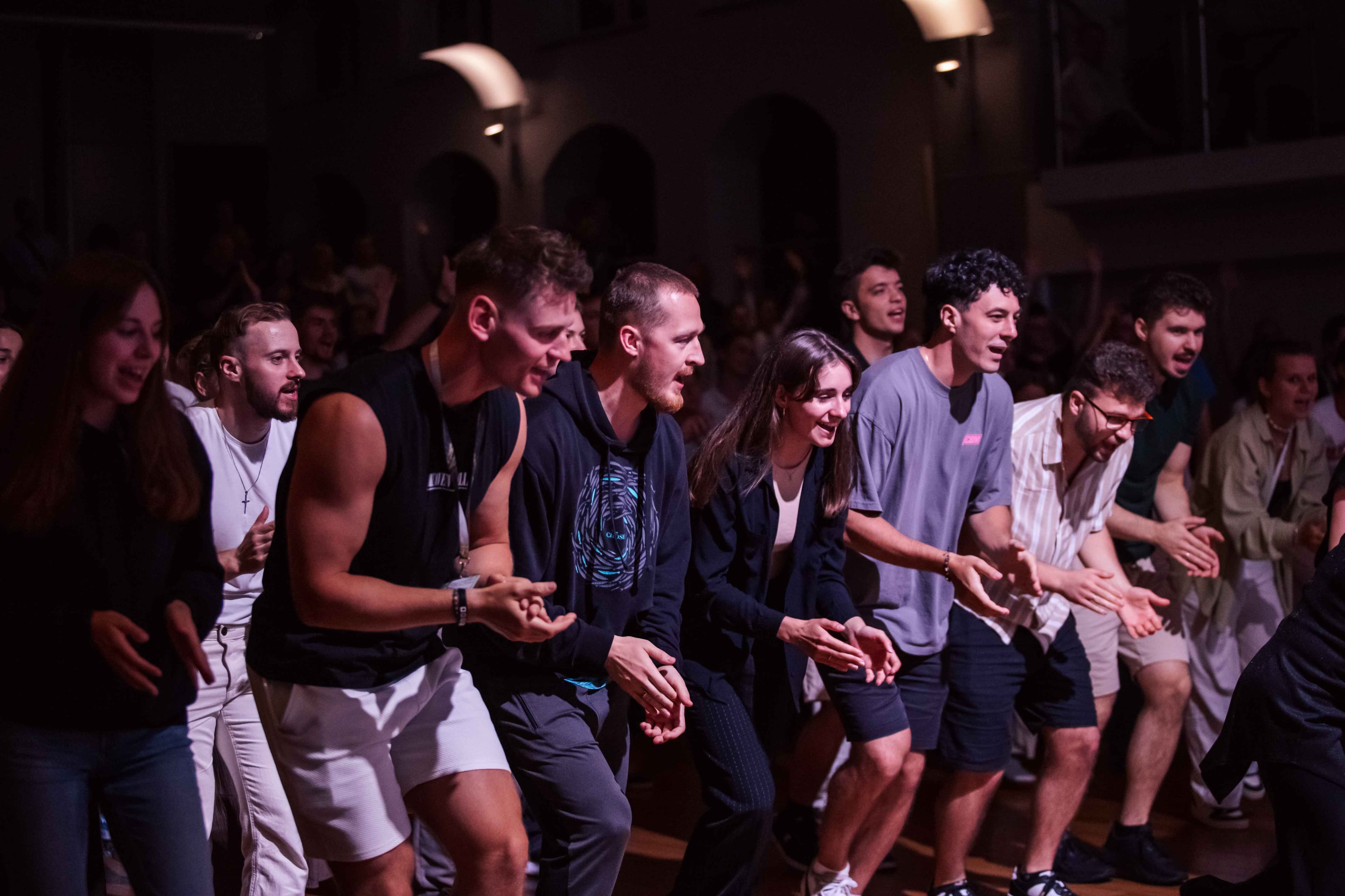 Obraz przedstawia ceremonię religijną w kościele. Na podwyższonej platformie stoi grupa duchownych w białych szatach liturgicznych, z centralną postacią w bogatszym ornacie, prowadząca rytuał przy ołtarzu ozdobionym białym obrusem i kwiatami. Na ołtarzu znajdują się świece i księga. W tle widoczny jest krzyż, a po bokach muzycy z instrumentami. Scena jest dobrze oświetlona, z ciepłą atmosferą.